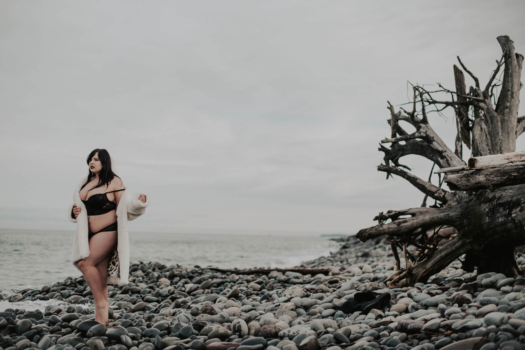 woman posing on cod rocky beach in white fur coat and black lingerie 