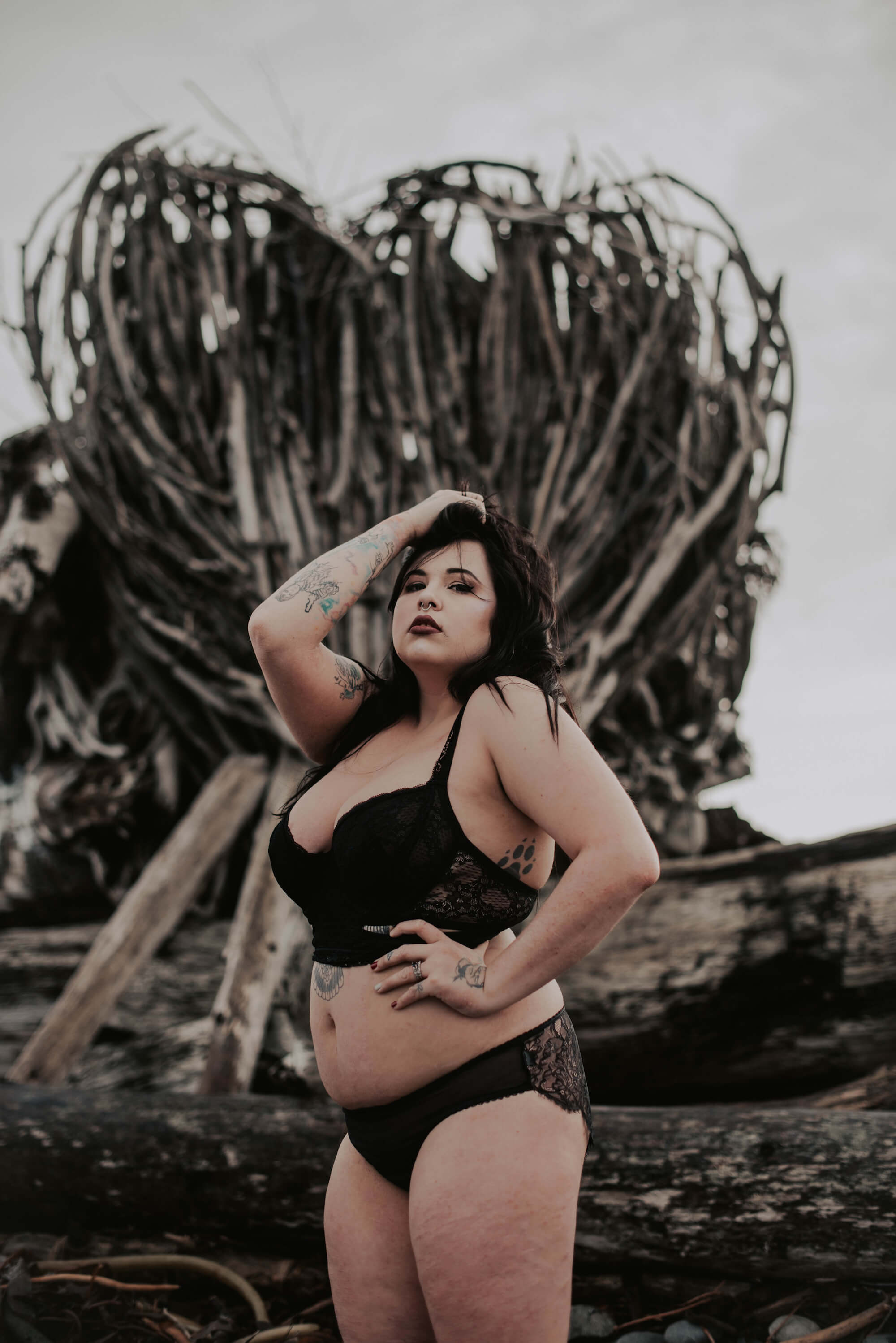 woman posing in black lingerie in front of wood stack shaped in a heart