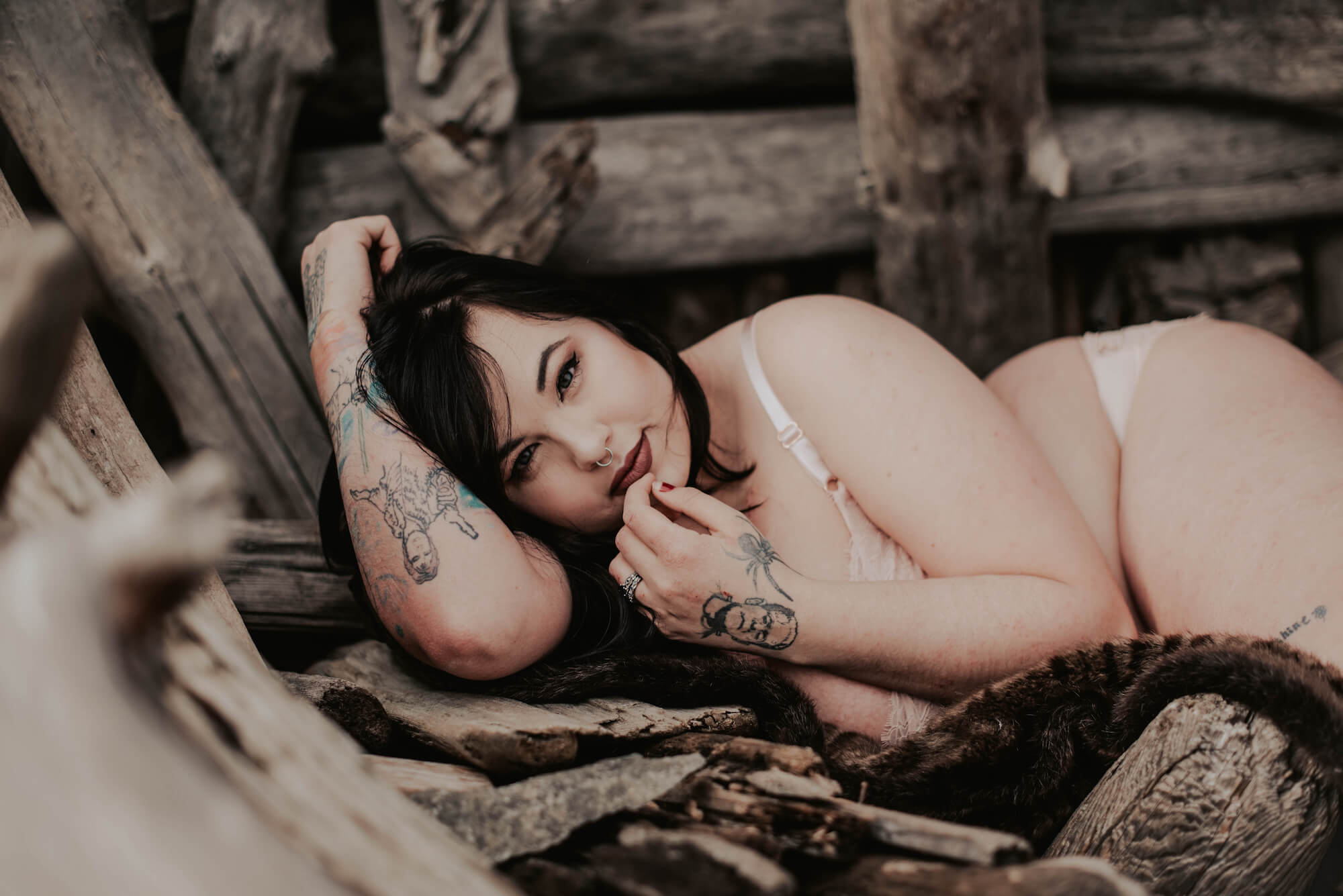 tattooed woman lying on brown fur coat on driftwood on pnw beach 