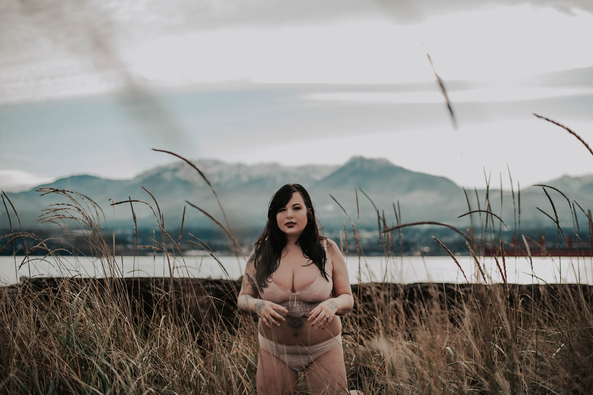 woman in pink underwear in front on mountain kneeling in tall grass