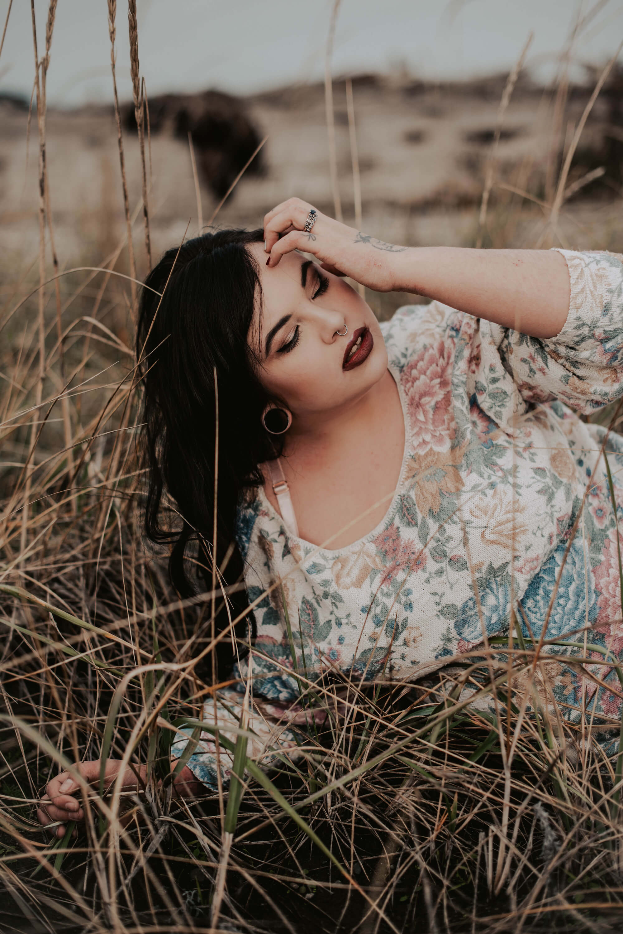 tattooed woman in sweater posing in tall grass