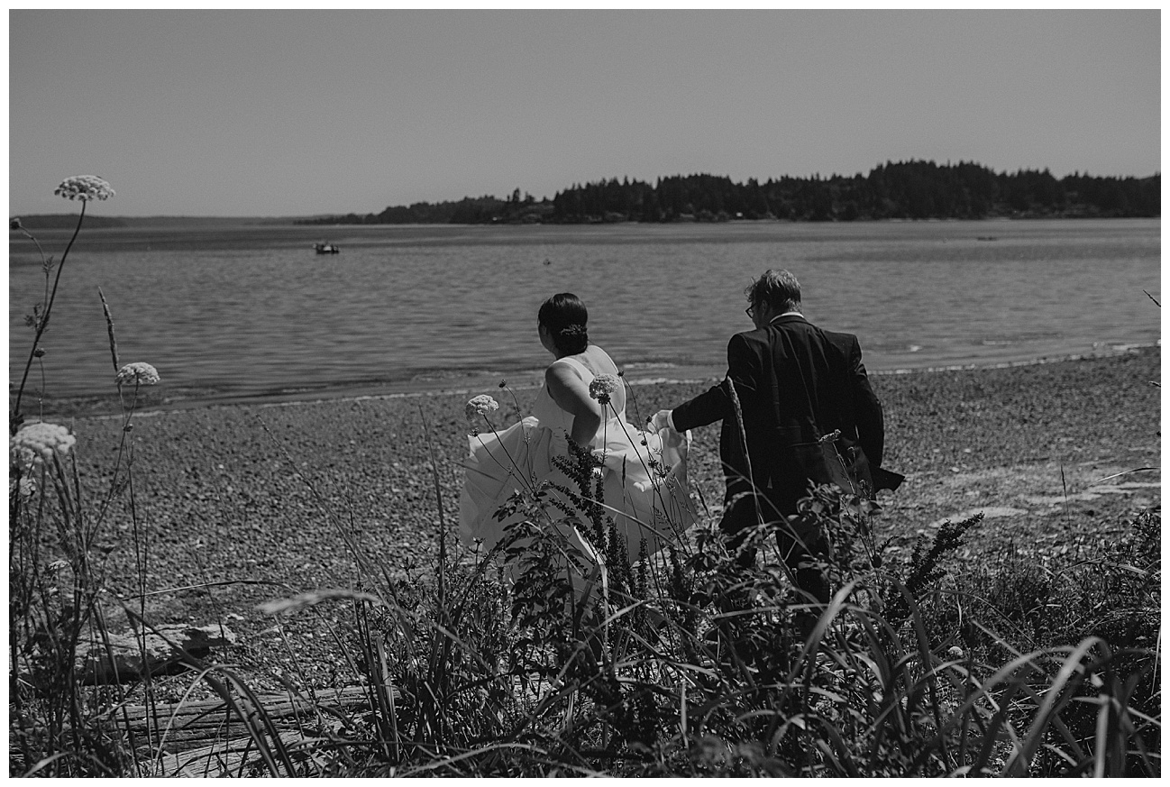 bride and groom walking on beach with flowers in the foreground 