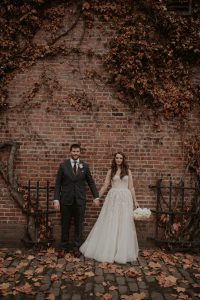 Bride and Groom in Pioneer Square Seattle posing in front of brick wall, bride holding an all white bouquet