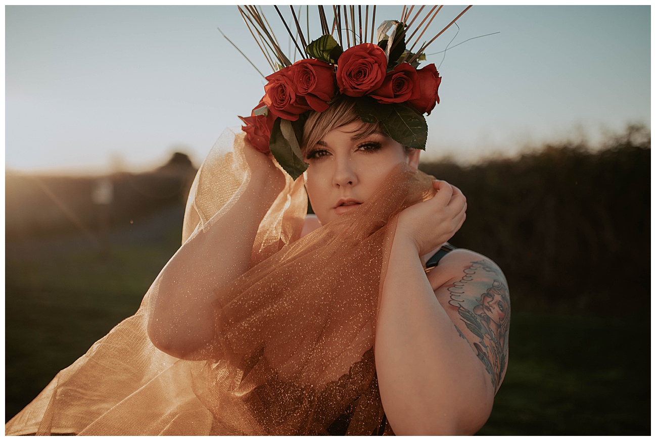 woman in golden hour light posing with sparkly fabric and a red rose flower crown