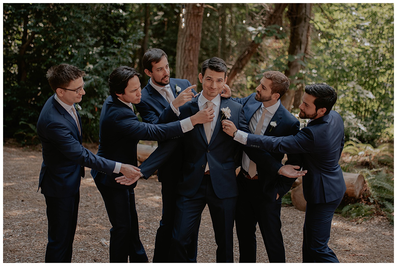 groomsmen in navy blue suits, surround the groom making sure her looks good