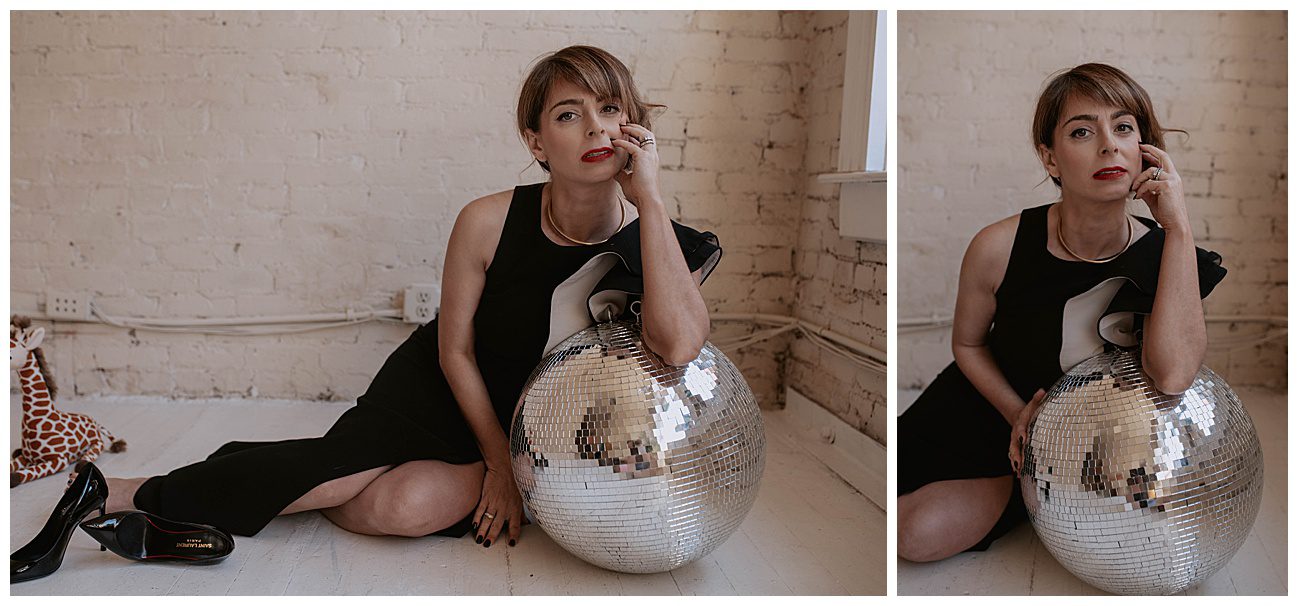 woman sitting on floor in full length black gown, leaning on a large disco ball