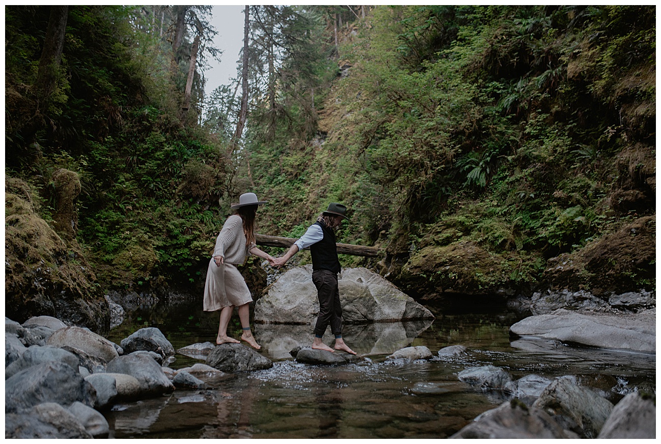 couple walking across rocks in river with matching hats for couples boudoir session