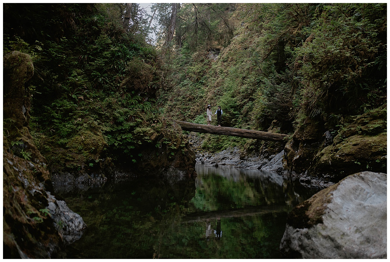 couple standing on log over river with their reflection in the water