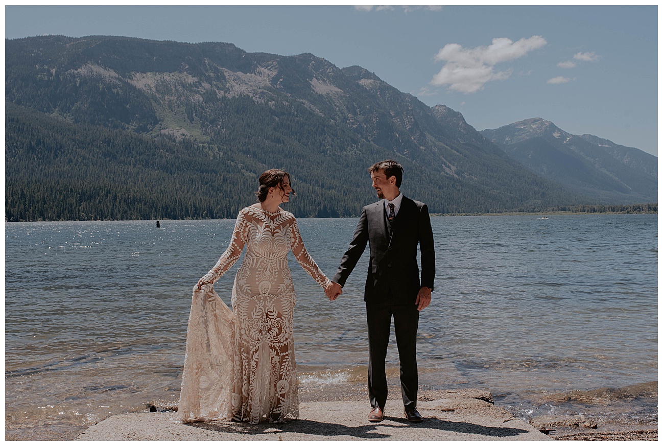 bride and groom hand in hand at edge of lake in Washington state 