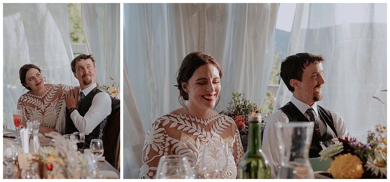 bride and groom sitting next to one another listening to wedding toasts laughing 